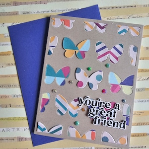 May include: A handmade card with a brown background and colorful paper butterflies. The card says "you're a great friend" in black letters.