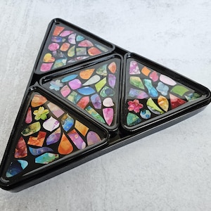 May include: A black serving tray with four triangular compartments. Each compartment is filled with colorful, mosaic-like designs of various shapes and sizes. The tray is made of a glossy material and sits on a light gray surface.