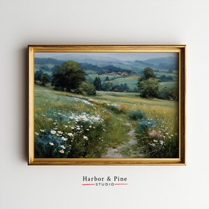 Puede incluir: Pintura de paisaje enmarcada que representa un camino de pradera que conduce a un pueblo. La obra de arte presenta un marco dorado y una escena serena con flores silvestres, árboles y colinas. El texto "Harbor & Pine STUDIO" está en la parte inferior.