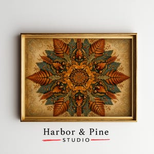 May include: A rectangular gold-toned frame containing a print of a symmetrical mandala-style design composed of orange and green fern leaves, acorns, and foliage. The text Harbor & Pine STUDIO appears in black below the framed artwork.