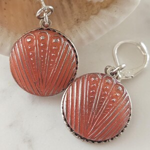 May include: A pair of silver dangle earrings with a round, orange, textured design. The earrings have a silver hook closure.