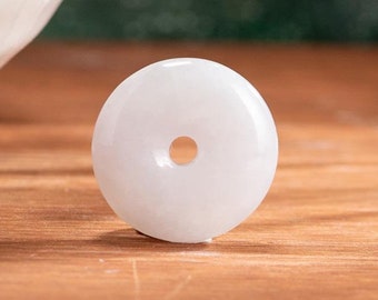 Op de afbeelding: Een witte, ronde jade hanger met een centraal gat, rustend op een houten oppervlak. De hanger is glad en gepolijst. De tekst "SUPER RICH" is zichtbaar onderaan de afbeelding.