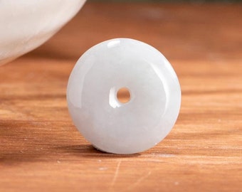 Op de afbeelding: Een witte jade hanger in de vorm van een munt met een gat in het midden. De hanger ligt op een houten oppervlak.