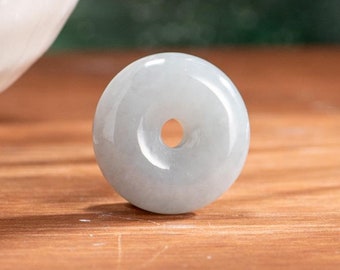 Op de afbeelding: Een lichtgroene jade hanger in de vorm van een donut met een gat in het midden. De hanger is glad en gepolijst.