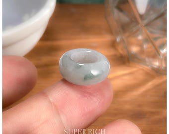 Op de afbeelding: Een lichtgroene jade ring met een glad, gepolijst oppervlak. De ring is rond en heeft een gat in het midden.
