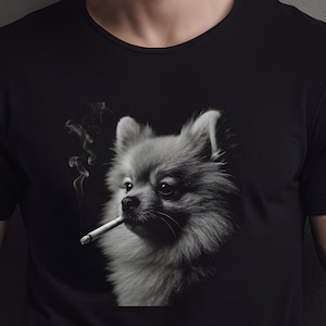 May include: Black t-shirt featuring a grayscale image of a Pomeranian dog smoking a cigarette. The dog's fur is detailed, and smoke curls upwards from the cigarette. The shirt is a solid black color.