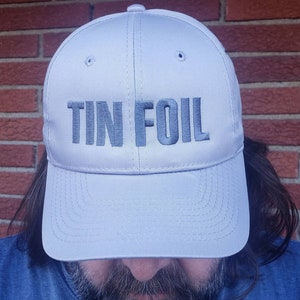 May include: A gray baseball cap with the text "TIN FOIL" embroidered in black on the front.