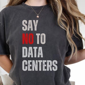 May include: Dark gray t-shirt with the text "SAY NO TO DATA CENTERS" in white and red letters. The shirt is a crew neck and has short sleeves. The shirt is worn by a person.
