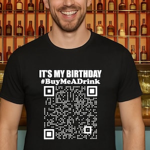 May include: Black t-shirt with the text "IT'S MY BIRTHDAY #BuyMeADrink" and a QR code. The person is wearing a party hat with colorful polka dots. The background features a bar with bottles.