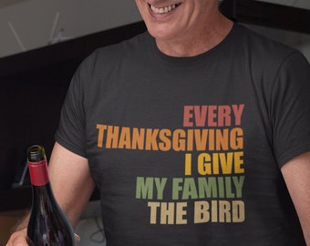 May include: A black t-shirt with the text "EVERY THANKSGIVING I GIVE MY FAMILY THE BIRD" in orange, yellow, green, and brown. The image shows a person holding a wine bottle and a wine glass, with a roasted turkey in the foreground.