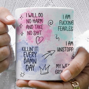 May include: White ceramic mug with a watercolor background and black text that reads "I will do no harm and take no shit", "I am fucking fearles", "I am killin' it every damn day", "I am unstopp", "My we grow", and other motivational phrases.