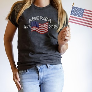 Close-up of dark heather grey t-shirt with rhinestone flag and “America 1776–2026” design.