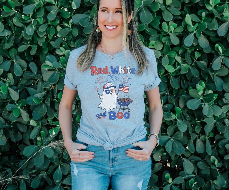 May include: A light gray t-shirt with the text "Red, White and Boo" and a cartoon ghost wearing sunglasses and a USA hat, holding a sparkler and American flag. The ghost is next to a barbecue grill.