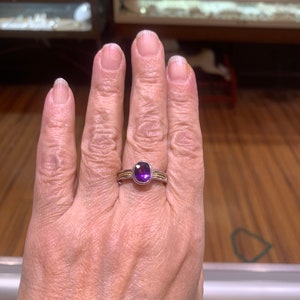 May include: A silver ring with a purple oval gemstone set in a gold band.