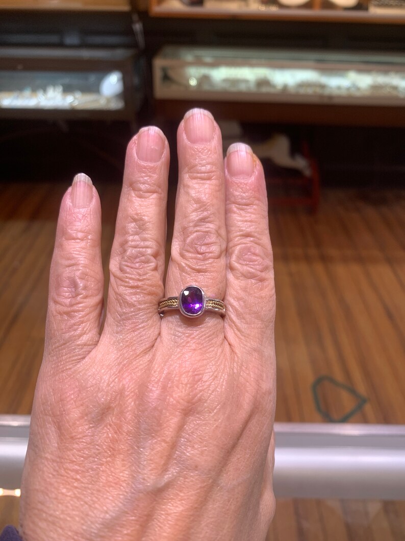 May include: A silver ring with a purple oval gemstone set in a gold band.