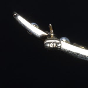May include: Close-up of a gold bracelet with a 14K hallmark. The bracelet is decorated with small white pearls.