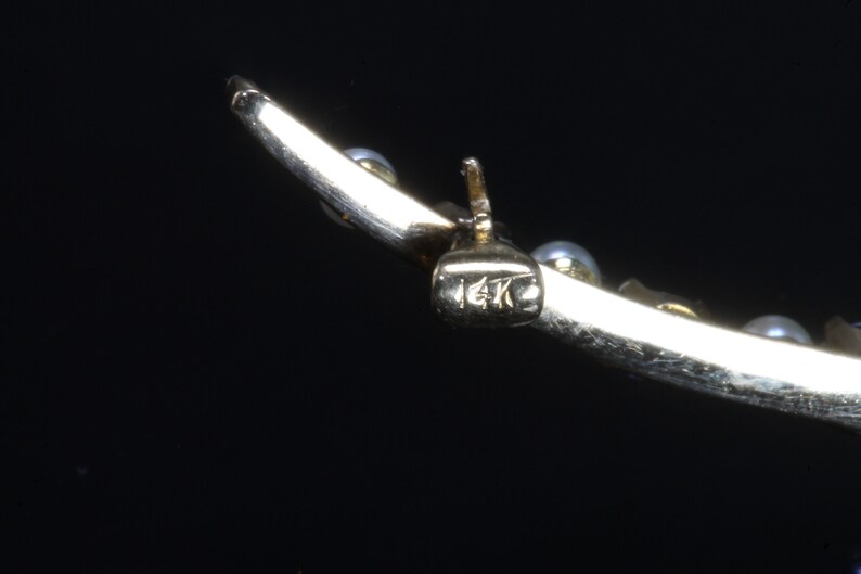 May include: Close-up of a gold bracelet with a 14K hallmark. The bracelet is decorated with small white pearls.