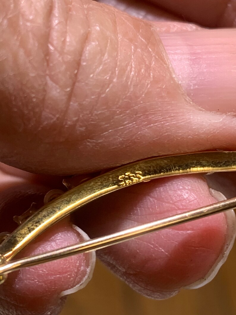 May include: A gold-toned brooch with a curved design and a pin closure. The back of the brooch is marked with the number "585".