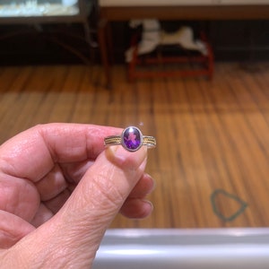 May include: A purple gemstone ring with a silver band and two thin gold bands.