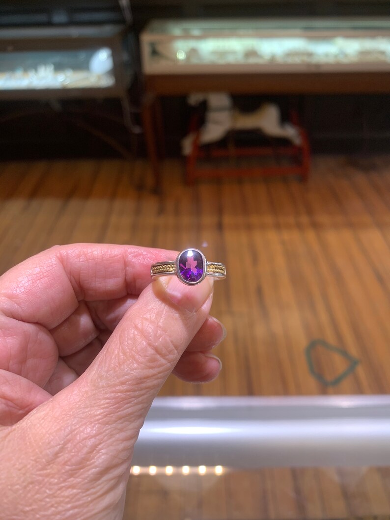 May include: A purple gemstone ring with a silver band and two thin gold bands.