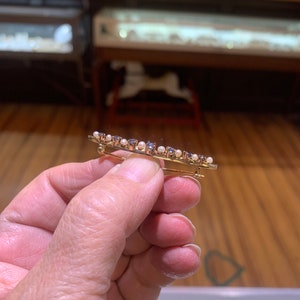 May include: A gold brooch with a row of small blue gemstones and white pearls.
