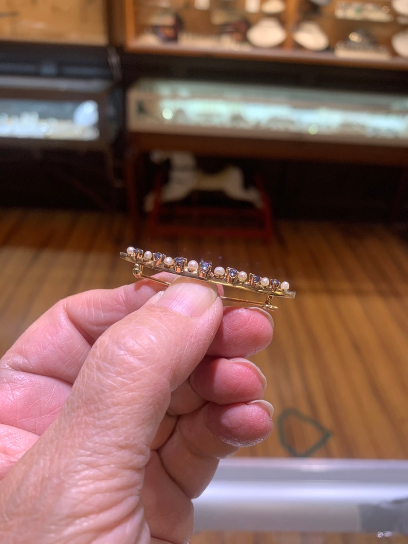May include: A gold brooch with a row of small blue gemstones and white pearls.