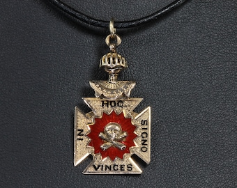 May include: A gold pendant with a red enamel cross and a skull and crossbones design. The pendant is inscribed with the words "Hoc Signo Vinces".