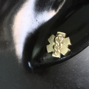 May include: Gold medical symbol earring with a snake wrapped around a star of life.