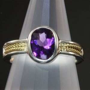 May include: A silver ring with a gold band and a large purple amethyst gemstone.