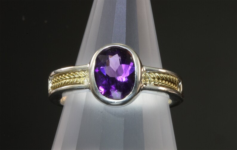May include: A silver ring with a gold band and a large purple amethyst gemstone.
