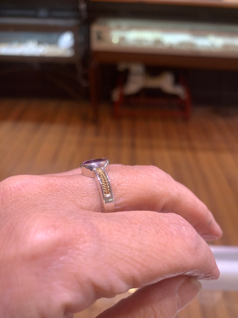 May include: A silver ring with a purple gemstone and a gold band with a braided design.