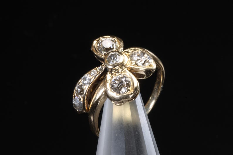 Puede incluir: Un anillo dorado con dise&ntilde;o floral, engastado con m&uacute;ltiples piedras preciosas transparentes. El anillo se muestra sobre un fondo negro, resaltando sus intrincados detalles y brillo. Una joya.