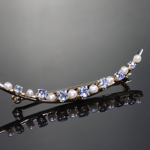 May include: A gold crescent-shaped brooch with blue and white gemstones. The brooch is set with small, round blue stones and white pearls.