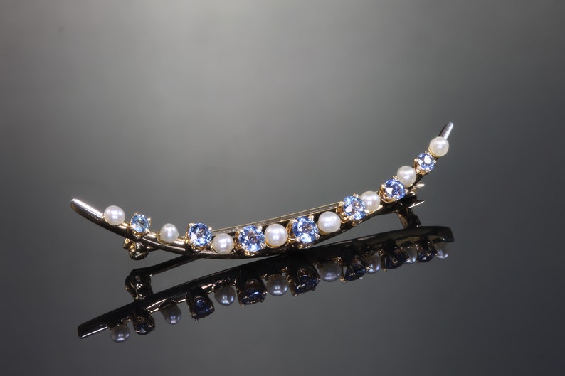 May include: A gold crescent-shaped brooch with blue and white gemstones. The brooch is set with small, round blue stones and white pearls.