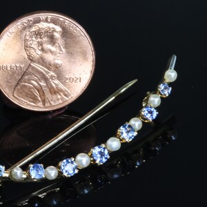 May include: A gold crescent-shaped brooch with alternating blue and white stones. The brooch is about the size of a US penny.