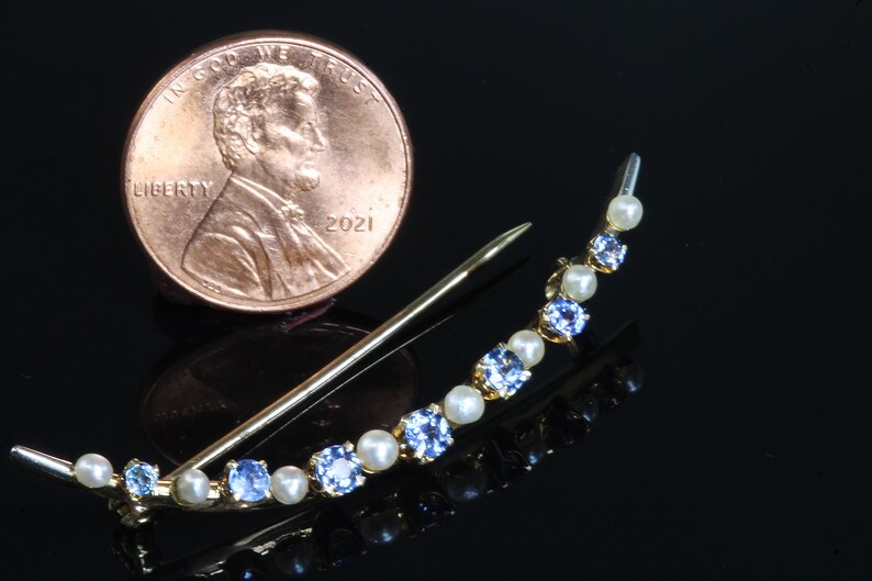May include: A gold crescent-shaped brooch with alternating blue and white stones. The brooch is about the size of a US penny.