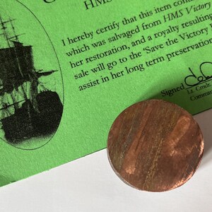 Op de afbeelding: Een echtheidscertificaat voor een stuk koper dat is geborgen van de HMS Victory, een historisch Brits oorlogsschip. Het certificaat is gedrukt op groen papier en bevat een zwart-wit afbeelding van het schip. De tekst op het certificaat luidt "Certificaat van HMS Victory Copper" en "Ik verklaar hierbij dat dit item koper bevat dat is geborgen van de HMS Victory, haar restauratie, en een royalty die voortvloeit uit de verkoop zal naar de 'Save the Victory' gaan om te helpen bij haar langetermijnbehoud." Het certificaat is ondertekend met "Getekend" en "Lt. Cmdr. Commar".