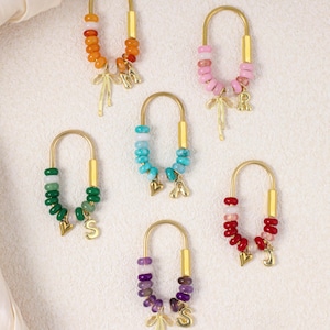 Peut inclure: Six porte-clés avec des cadres en métal doré en forme de U. Chaque porte-clés présente une couleur différente de perles, dont orange, rose, bleu, vert, rouge et violet. Chaque porte-clés a un charme doré avec une lettre.