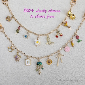 May include: Gold-toned charm necklaces with various pendants, including a horseshoe, crown, heart, and sunflower. The image includes the text "800+ Lucky charms to choose from". The charms are colorful and detailed, with a variety of shapes and designs.