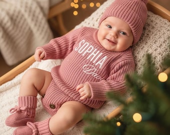 Puede incluir: Un bebé con un conjunto de punto rosa a juego, que incluye un gorro con pompón, un pelele y patucos. El pelele tiene bordado el nombre "SOPHIA Davis" en blanco. El bebé está tumbado sobre una manta blanca.