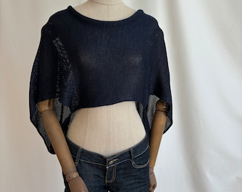 May include: A dark navy blue knit crop top featuring a wide boat neckline and short, loose-fitting sleeves. The garment has a high-low hemline with a shorter front and longer back, crafted from a lightweight, semi-sheer textured knit fabric.