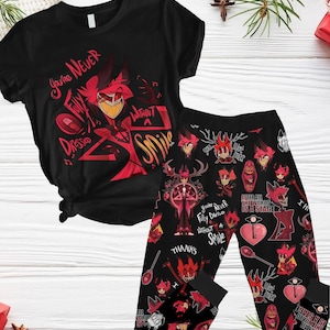 Könnte beinhalten: Schwarzer und roter Pyjama-Set mit einer Comicfigur mit roten Hörnern und einem roten Anzug. Das Oberteil hat den Text "You're Never Fully Dressed Without A Smile" und die Hose hat ein sich wiederholendes Muster der Comicfigur und den Text "You're Never Fully Dressed Without A Smile".