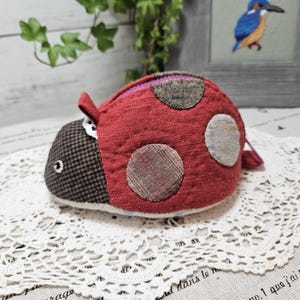 May include: A red ladybug-shaped coin purse with brown and white polka dots. The purse is made of fabric and has a zipper closure.
