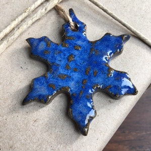 May include: A blue and brown ceramic snowflake ornament with a rustic glaze. The snowflake has a hole at the top for hanging.