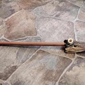 May include: A unique, handcrafted pipe featuring a wooden stem and a carved alligator head bowl. The alligator head is a natural tan color, and the pipe has a light brown wooden stem.
