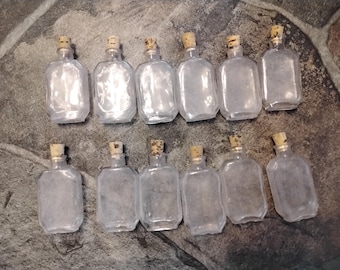 May include: A collection of 13 clear glass bottles with cork tops. The bottles are all the same size and shape, and they are arranged in two rows.