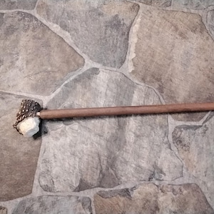 May include: A handcrafted wooden pipe with a deer antler bowl. The pipe features a long, slender, brown wooden stem and a textured antler bowl. The pipe is set against a stone background.