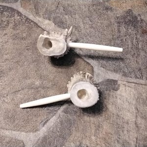 May include: Two antler bottle stoppers with white stems. The stoppers have a natural, textured appearance, with a circular opening in the center. The white stems extend from the antler base.