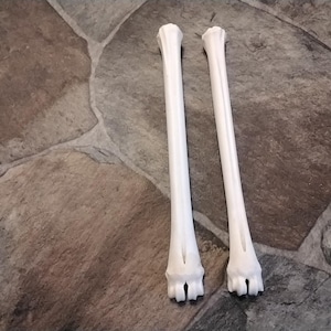 May include: Two white, elongated, cylindrical objects with textured, multi-pronged ends. These items feature a smooth, matte finish and a straight, uniform structure, resembling the appearance of long, slender bones or specialized structural components.