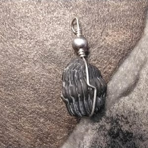 May include: A black stone pendant with a silver wire wrap and a silver bead. The pendant is hanging from a silver wire loop.